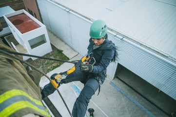 Female firefighter rescuer beginning the descent of a huge wall using the rappelling device in a multi-story building.