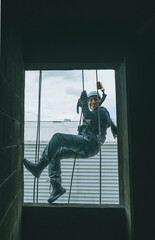 Female firefighter rescuer descending a huge wall with the rappelling device in a multi-story building, hanging from a window.