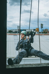 Female firefighter rescuer descending a huge wall with the rappelling device in a multi-story building, hanging from a window.