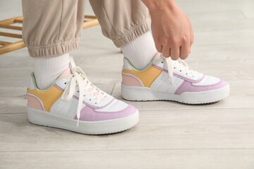 Woman tying shoelace of colorful sneaker indoors, closeup