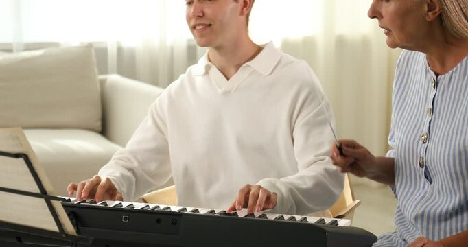 Tutor teaching man to play piano indoors. Zoom in