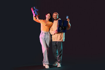 Fototapeta premium Young couple with credit card and gifts on dark background. Cyber Monday
