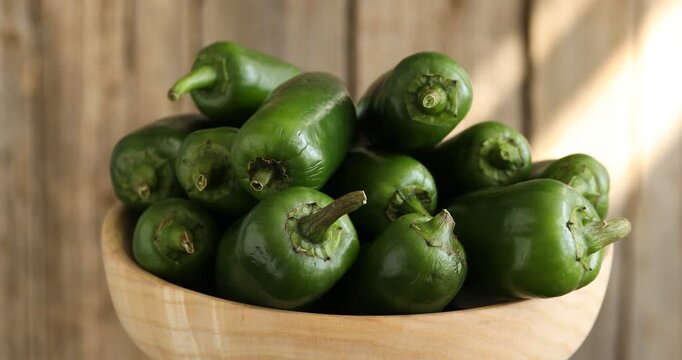 Ripe green jalapeno peppers in bowl on wooden background, spinning