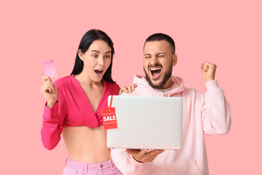 Happy young couple with credit card and laptop on pink background. Cyber Monday