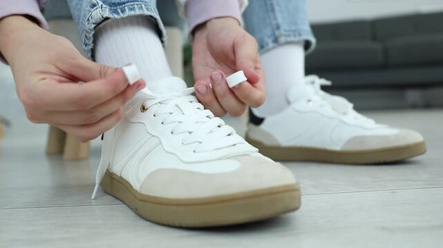 Woman tying shoelace of white sneaker indoors, closeup