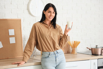 Beautiful young woman with glass of milk in kitchen