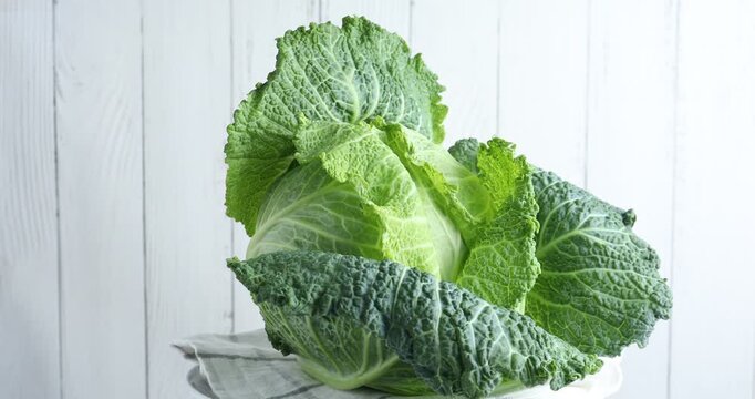 Fresh Savoy cabbage spinning near white wall