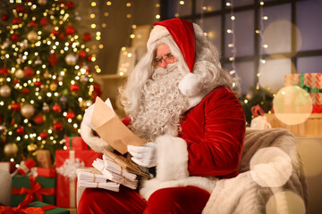 Santa Claus with letter in armchair at home on Christmas eve