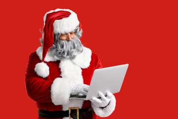 Santa Claus using laptop on red background