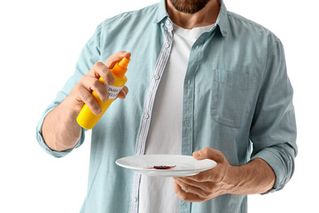 Young man spraying cockroach on plate with insect repellent against white background, closeup