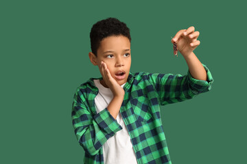 Scared African-American boy with cockroach on green background