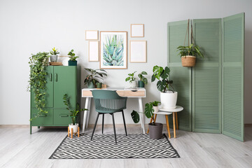 Interior of stylish office with workplace, blank frames and houseplants