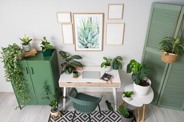Interior of stylish office with workplace, blank frames and houseplants