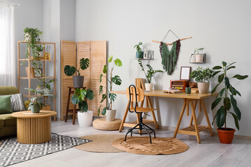 Interior of light office with workplace, folding screen and houseplants
