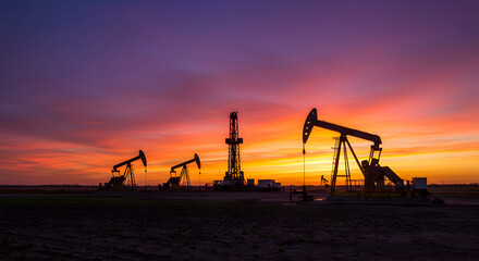 Oil Rig Derricks Silhouetted Against A Sunset Sky Over A Tranquil Field