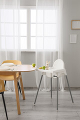 Baby highchair with fruits and toy in dining room interior