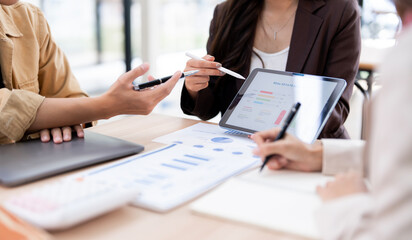 A high-angle shot of a business team collaborating on a project, focusing on their hands and a laptop screen displaying data. Professional discussion, and the process of analyzing business reports.