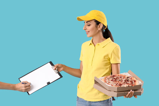 Female courier with tasty pizza and hand signing in clipboard on blue background - Powered by Adobe