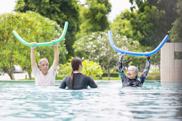 Trainer with Senior Asian Couple Exercising in a Swimming Pool, Happy Elderly People Doing Aqua Aerobics with Pool Noodles, Active Retirement, Cheerful Senior Couple Enjoys Water Exercise