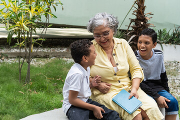 Grandmother laughing with grandchildren reading a book outdoors