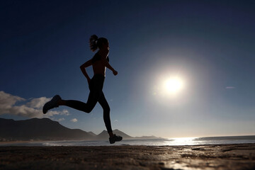 Silhouette of determined woman running on coastal landscape at sunrise