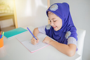Happy Muslim girl in a purple hijab writing in her notebook at a white desk, with colorful pens beside her. Concept of education, creativity, and childhood development. she doing homework.