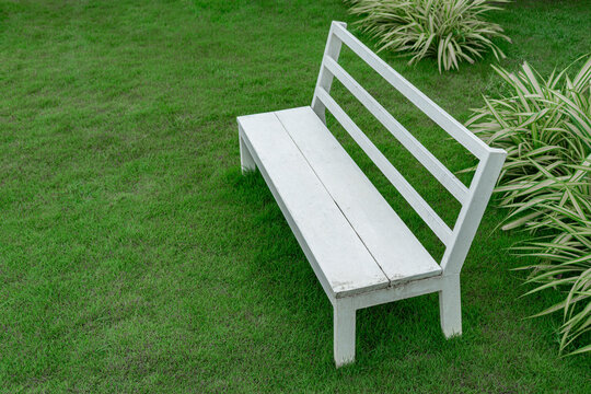 Bench made from steel and artificial wood it's white painted lay on the space of lawn at the garden
