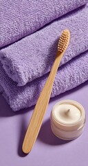 A bamboo toothbrush rests on a lilac background beside a small jar of cream and a stack of fluffy lilac towels