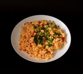 Fried egg omelette with tomato in a round ceramic plate decorated with parsley and green onions on a black background.