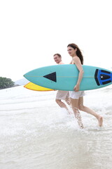 Couple lover running on beach with surfboards, splashing water and smiling under summer sunlight, concept of  friendship, vacation, holidays, surfing, freedom, and fun tropical lifestyle.
