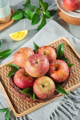Fresh Red Apples in Wicker Basket with Green Leaves on Kitchen Table