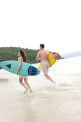 Fototapeta premium Couple lover running on beach with surfboards, splashing water and smiling under summer sunlight, concept of friendship, vacation, holidays, surfing, freedom, and fun tropical lifestyle. 