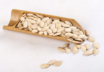 Raw pumpkin seeds in wooden scoop spilling on white background - healthy cooking ingredient