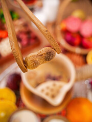 Bamboo kitchen tongs picking up peanut with fresh produce in blurred background