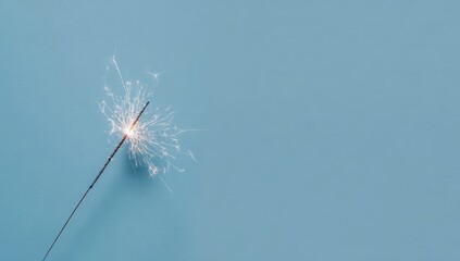 Obraz premium A single lit sparkler against a solid pale-blue background, its bright sparks radiating outwards, leaving ample negative space to the right