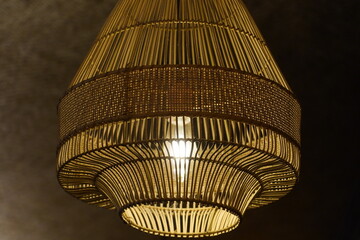 A beautifully crafted, handmade bamboo or rattan pendant lamp hangs from the ceiling, its warm, glowing light creating a cozy and inviting atmosphere. The intricate, natural weave of the shade casts s