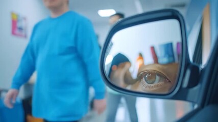 Eye reflects in car mirror inside, blurred figure walks by