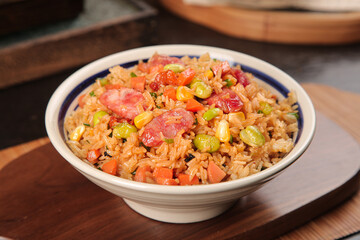 Delicious fried rice with vegetables and meat in ceramic bowl on wooden table