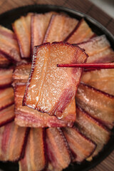 Wood-fired smoked bacon in cast iron pan with chopsticks - traditional farmhouse cooking for New Year's Eve