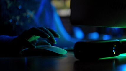Close-up of a person using a gaming mouse with RGB lighting next to a keyboard in a dark room with neon red light - Powered by Adobe