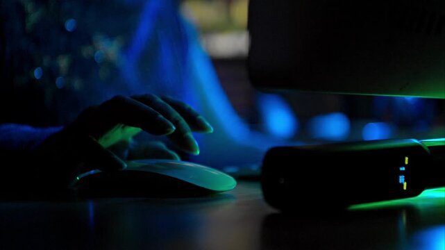 Close-up of a person using a gaming mouse with RGB lighting next to a keyboard in a dark room with neon red light