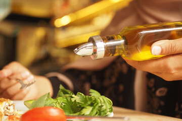 Person drizzling olive oil over a fresh salad