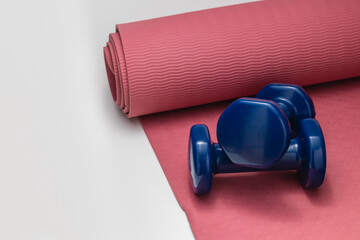 Blue dumbbells placed on a pink yoga mat, representing home workout, fitness, and healthy lifestyle