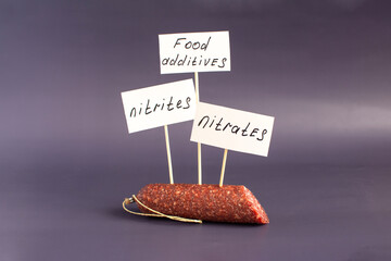 A fragment of smoked sausage in a package and the warning labels "nitrites" and "nitrates" in close-up on a dark background