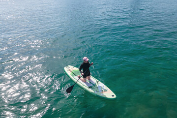 Fototapeta premium Young woman sitting on sup board and holding an oar at sea.
