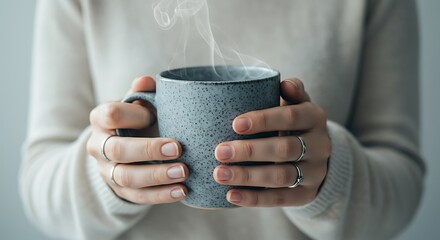 Close-up of hands holding a steaming mug of hot beverage, cozy comfort