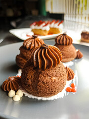 Chrunhy choux with chocolate.
A close-up of an elegant chocolate profiterole dessert. The choux pastry puffs are topped with a rich, piped chocolate cream and a dusting of cocoa. 