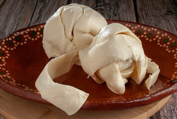 Mexican cheese called QUESILLO made in Oaxaca, on a handmade Mexican clay plate, on a rustic wooden table, side view