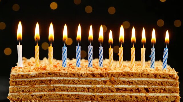 Honey layer cake with ten burning candles on a black background decorated with lights for a birthday party or celebration.