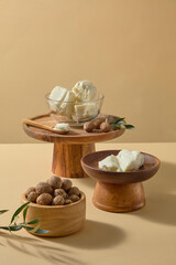 Natural ivory shea butter pieces, green sprig and scattered nuts styled on a beige surface, suitable for handmade soap, spa, and organic body butter visuals. Front view, vertical frame for social a